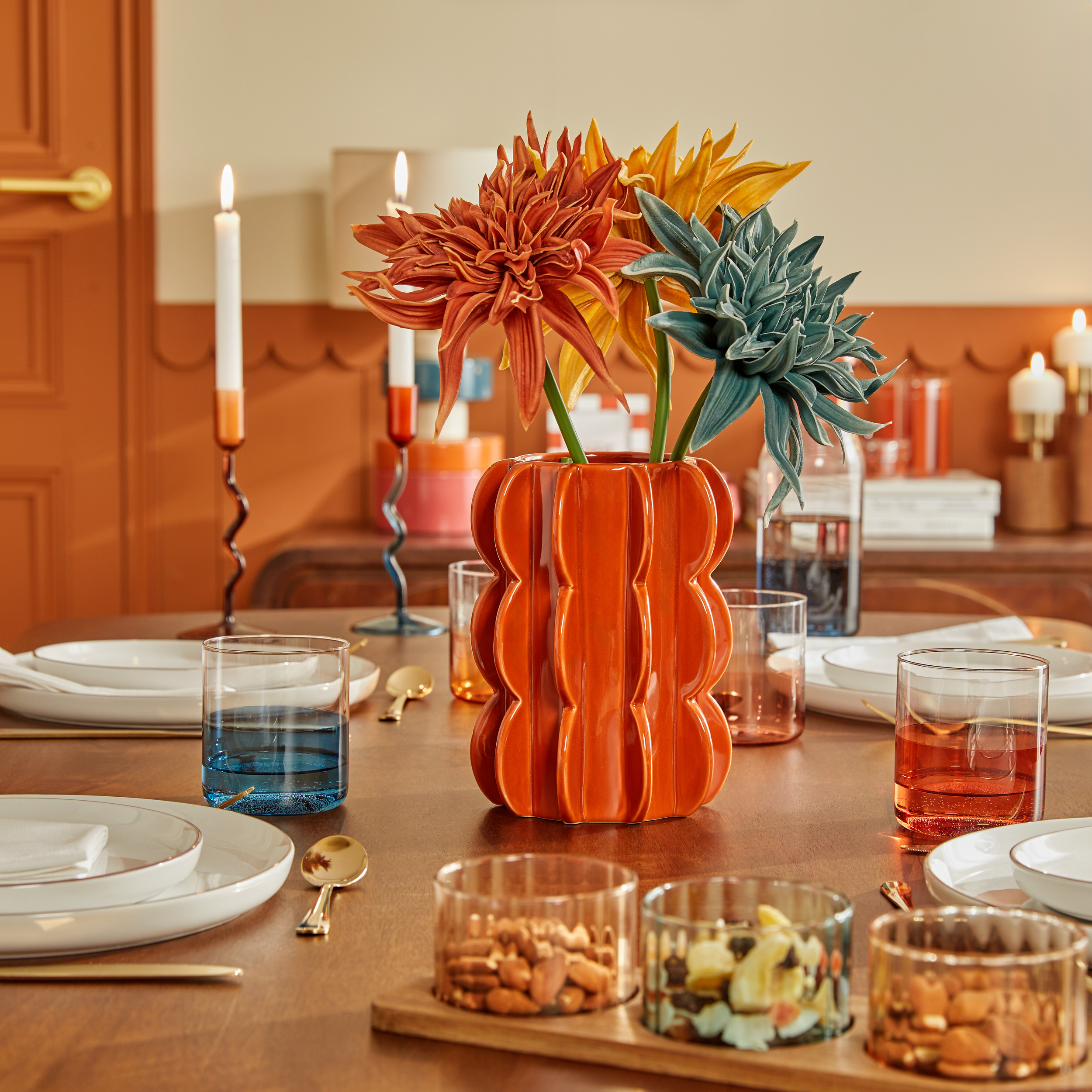 Vase orange posé sur table à manger en bois avec larges fleurs dedans