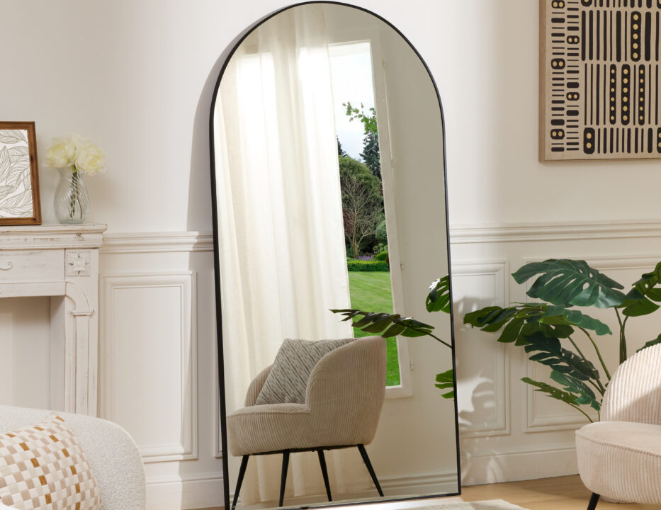 grand miroir arche noir posé au sol dans un salon contemporain avec fauteuil beige et plante verte