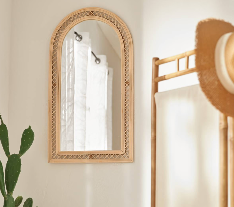 miroir arche en rotin tressé dans une entrée bohème avec porte-vêtements en bambou et cactus