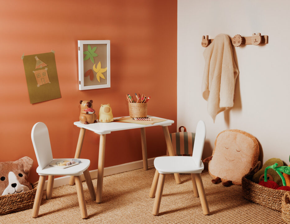 mesa infantil con dos sillas blancas de madera en una habitación decorada en tonos terracota con accesorios y juguetes
